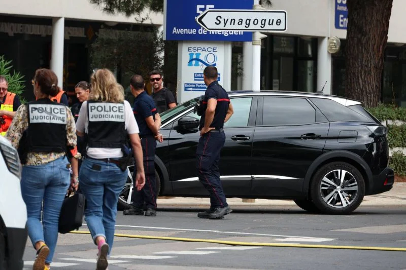 Des officiers de police judiciaire français passent devant des pompiers après l'incendie et l'explosion de voitures dans une synagogue